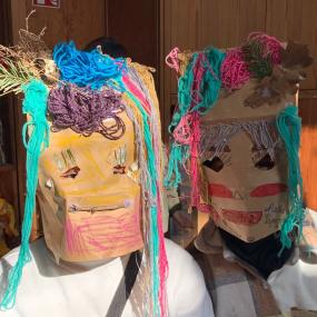 Zwei Kinder haben Masken aus bunter Wolle auf.