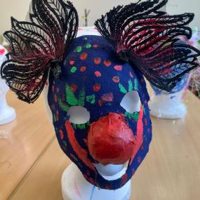Eine dunkelblaue Maske mit roter Clownsmaske und zwei großen Ohren aus schwarzer Spitze. 