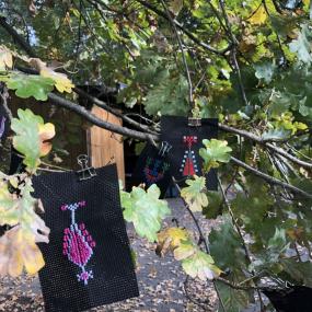 Zwei fertige Stickereien hängen an einem Ast im Baum. 