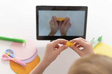 Ein Junge knetet gelbe Knete und filmt dabei seine Hände durch ein Tablet.