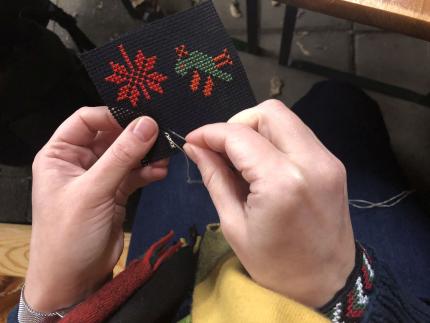 Hände sticken ein Muster mit bunten Garn auf schwarzen Untergrund.